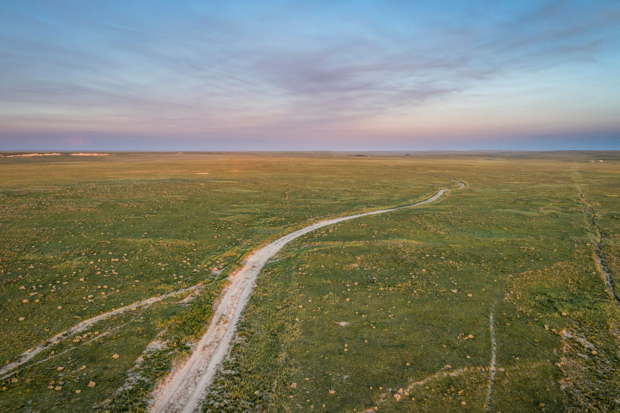 An aerial view of a two-track road across green prairie